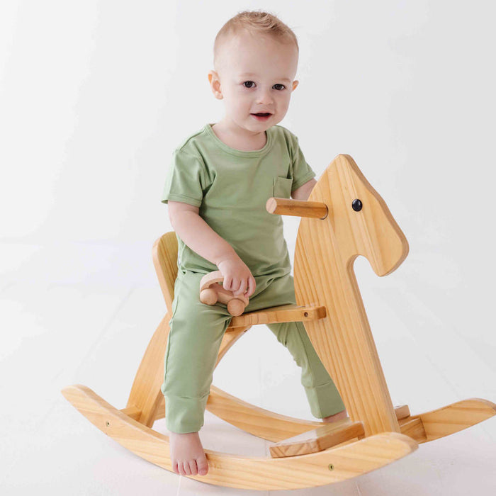 Child in green outfit sitting on a wooden rocking horse against a white background