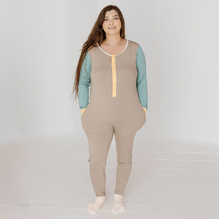 A woman modeling a beige color-blocked jumpsuit with sage green long sleeves and a pale yellow front placket, set against a bright white studio background.
