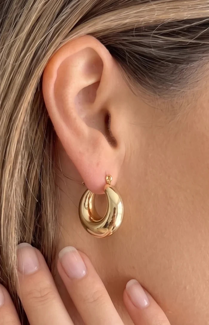 Close-up of a highly polished gold chunky puffed hoop earring with a hollow interior curve