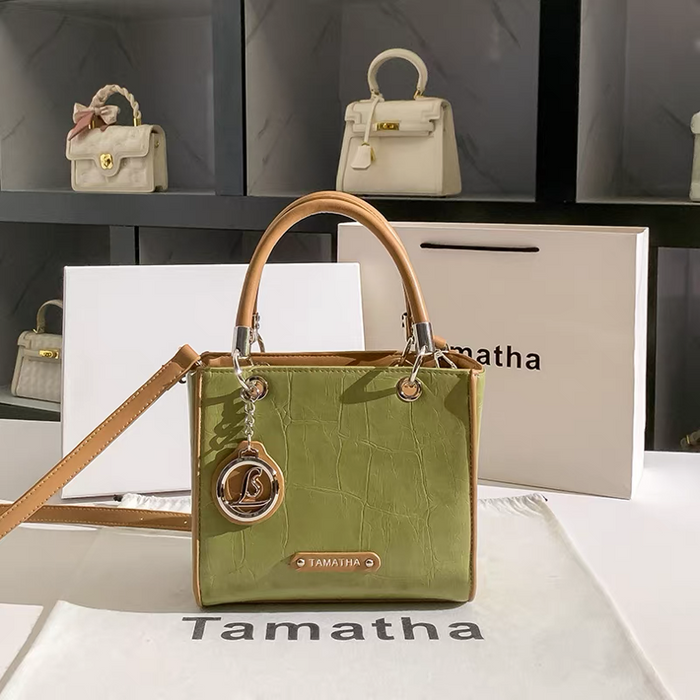 Green handbag with brown handle and strap on a white surface with 'Tamatha' branding.