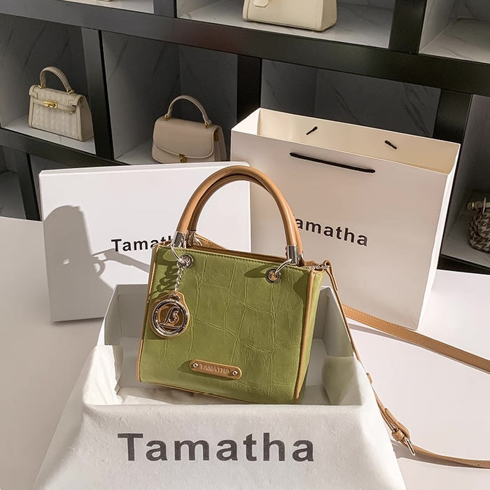 Green handbag with brown handle and strap on a white surface with 'Tamatha' branding.