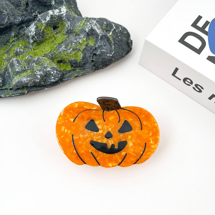An orange jack-o'-lantern-shaped accessory with black facial features, photographed on a white surface with a dark textured stone and part of a white book visible in the background.