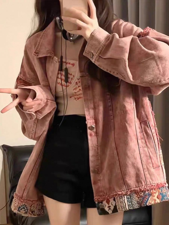 Person wearing a pink denim jacket with colorful patchwork details, sitting on a chair.