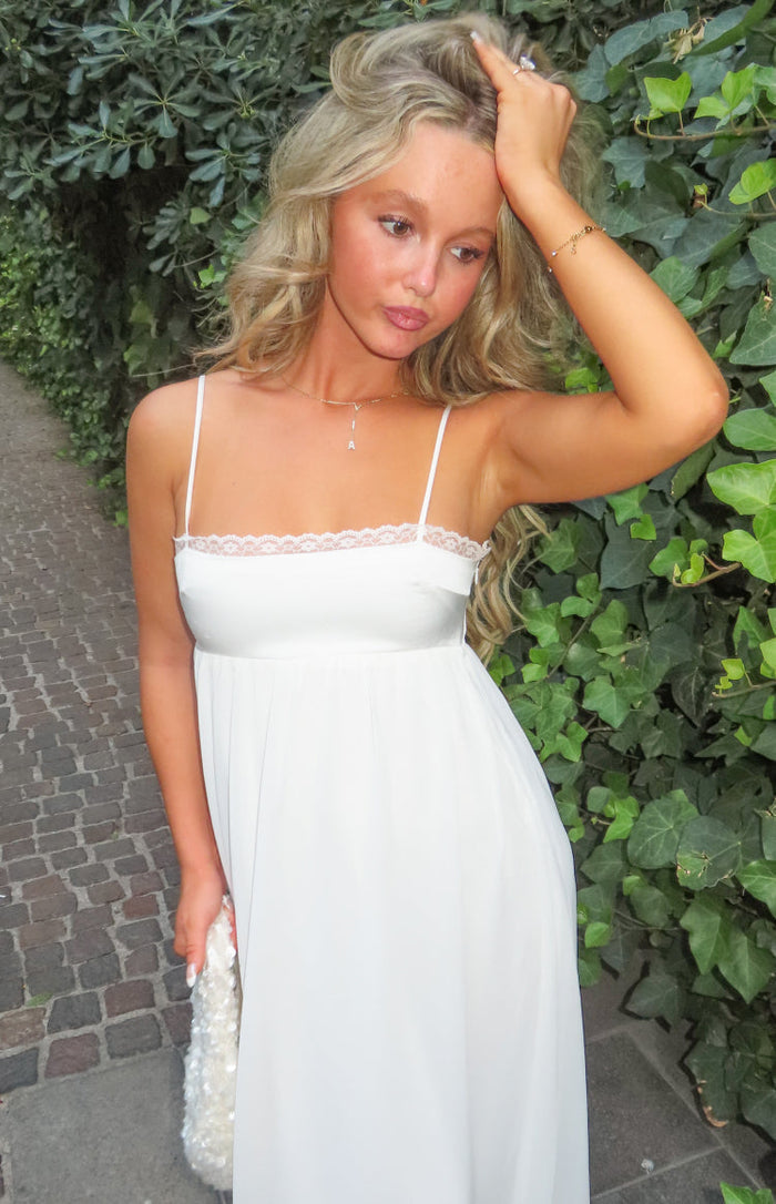 Close-up of the white satin maxi dress showing the delicate lace trim along the straight neckline and thin spaghetti straps