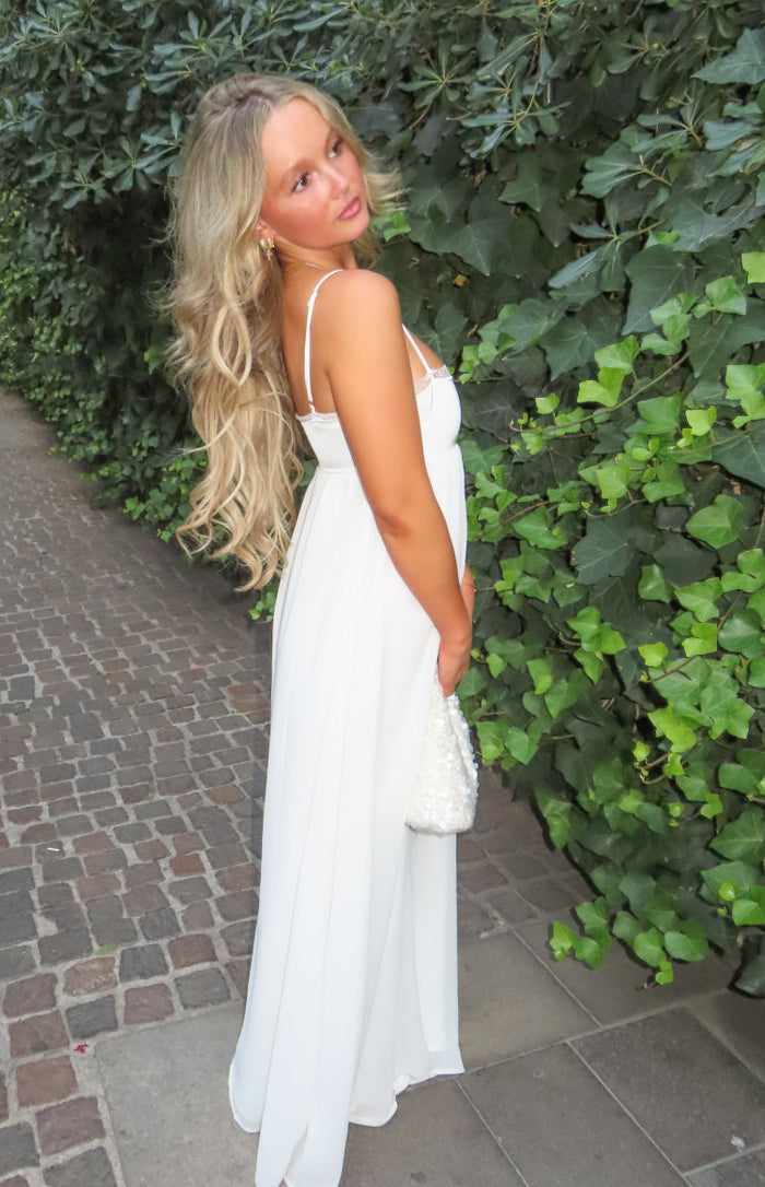 Side view of a white satin maxi dress with thin spaghetti straps, lace trim bust, and a flowing empire waist