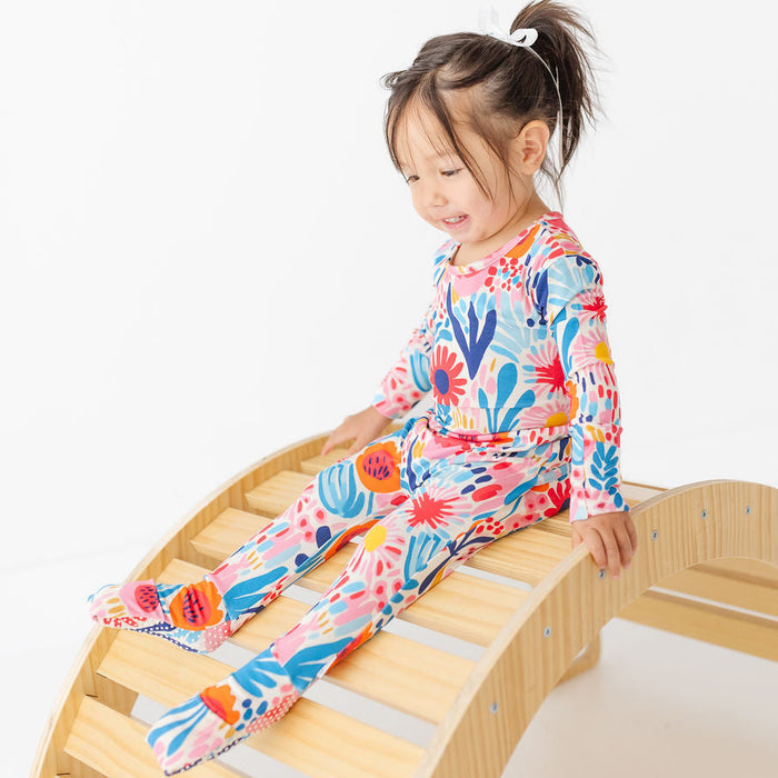 Child in a colorful outfit sitting on a wooden climbing toy against a white background