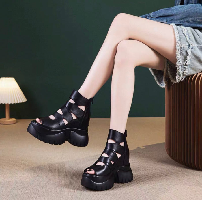 Person wearing black platform sandals with cut-out design on a neutral background