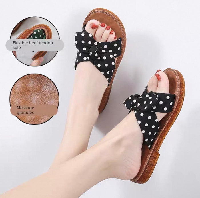 Black polka dot sandals with bows worn by a person on a light gray background