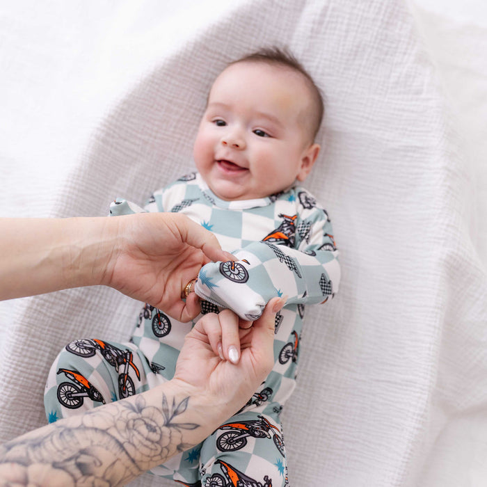 Baby wearing a patterned onesie with a person holding their hand, all on a white background.