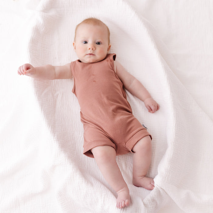 Baby in a pink romper lying on a white blanket