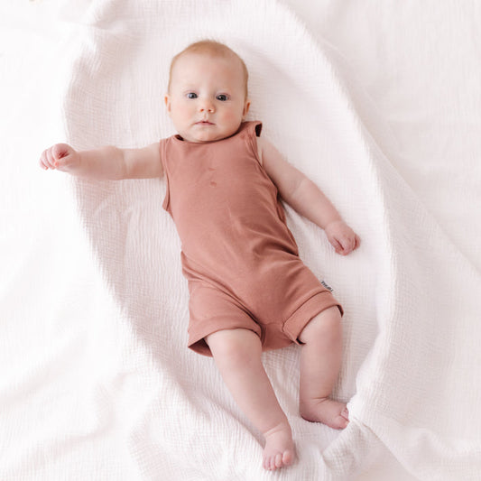 Baby in a pink romper lying on a white blanket