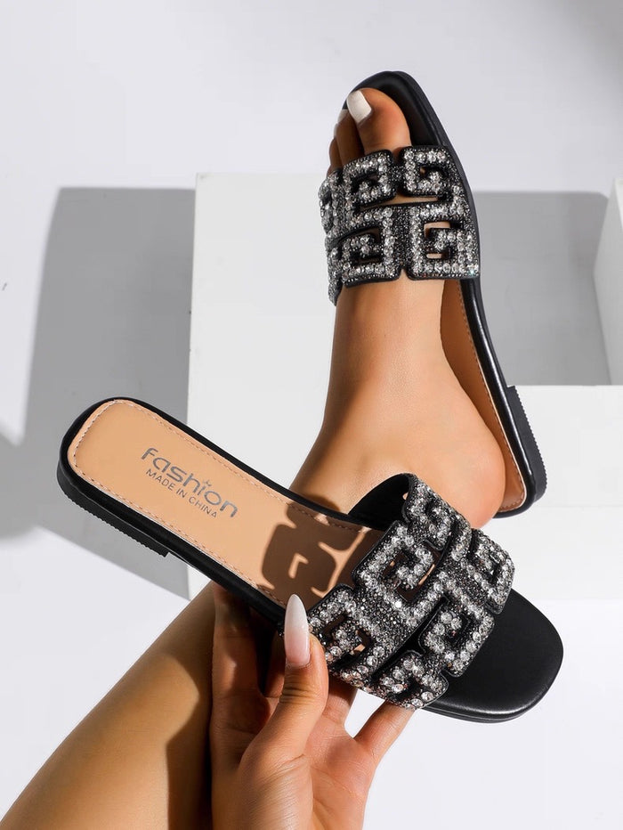 Black slide sandals with decorative straps held by a hand on a light background