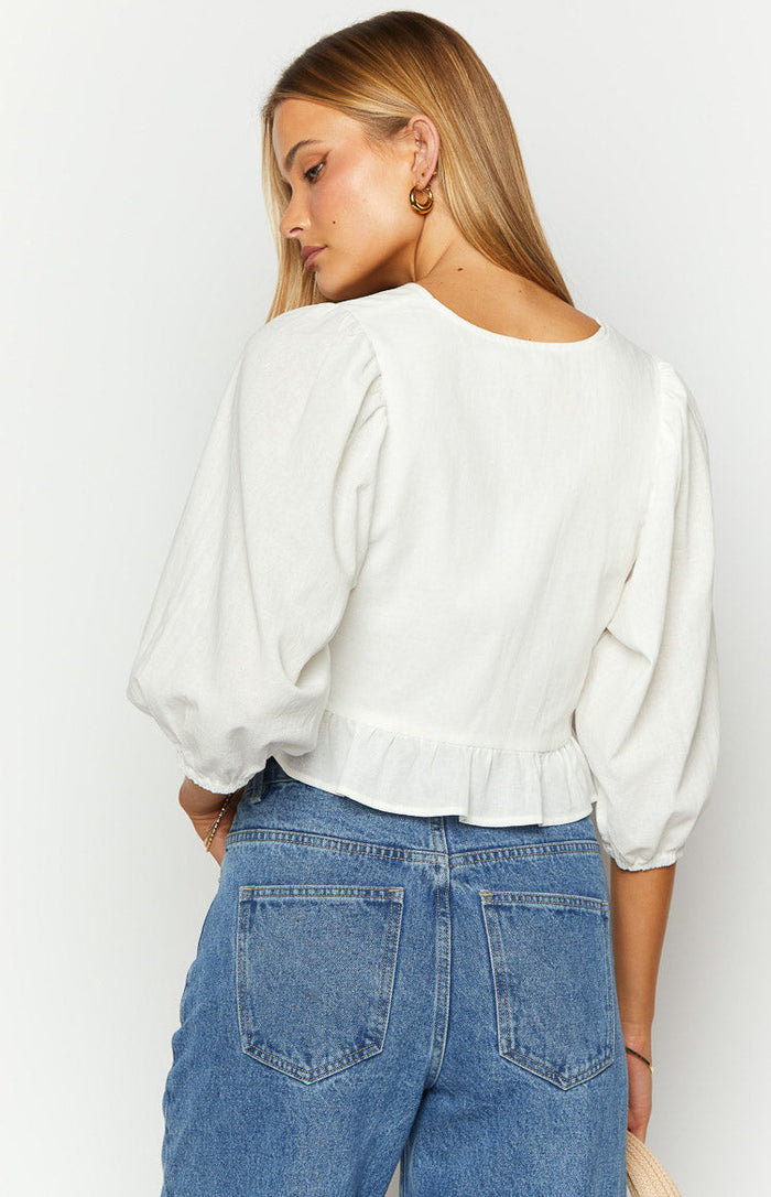 White tie-up top with multiple front bows, a chest cutout, ruffled hem, and elbow-length puff sleeves