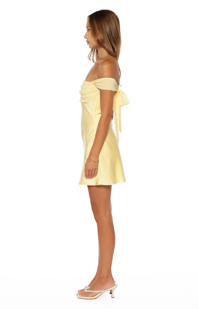 Side view of a yellow off-the-shoulder mini dress with a ruched bodice and a large bow tie at the back