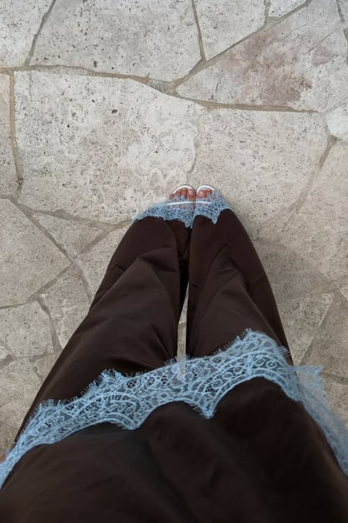 Close-up of the light blue scalloped lace trim on the hem of brown satin pants
