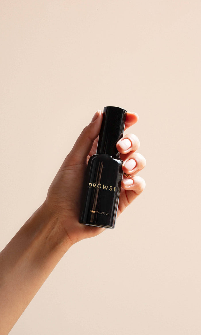 Hand holding a black bottle labeled 'Drowsy' against a beige background
