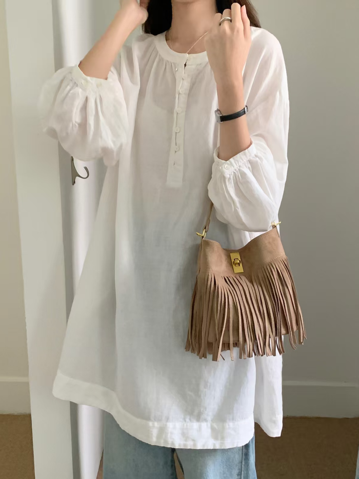 Beige suede-look microfiber crossbody bucket bag with relaxed fringed silhouette worn with a white blouse