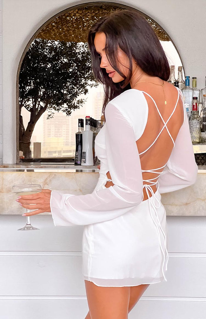 Rear view of a white mini dress with sheer long sleeves, an open back with criss-cross straps and tie detail