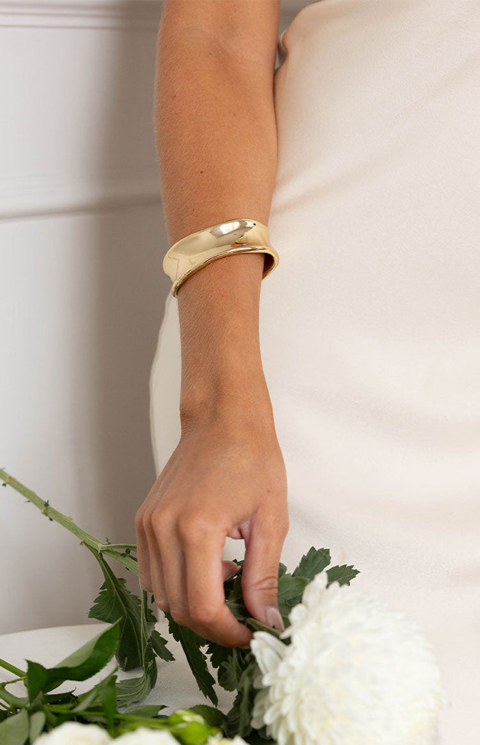 Polished gold cuff bangle with a distinct wavy, sculptural design