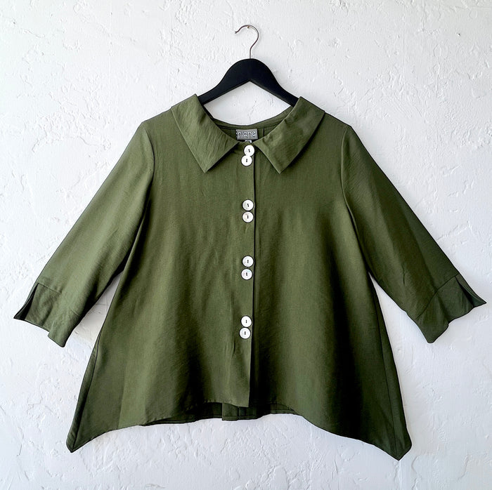Green blouse with white buttons on a hanger against a white wall