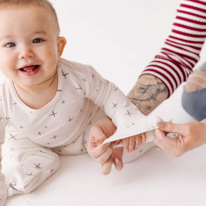 Baby sitting on a white floor with a person holding a piece of paper.