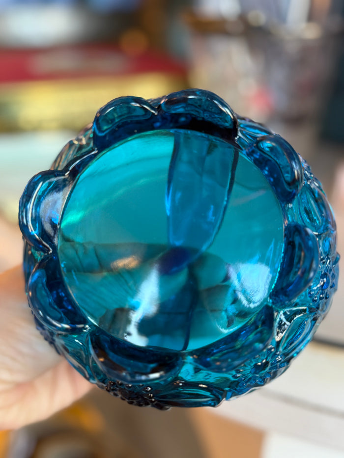Blue decorative object held by a hand with a blurred background