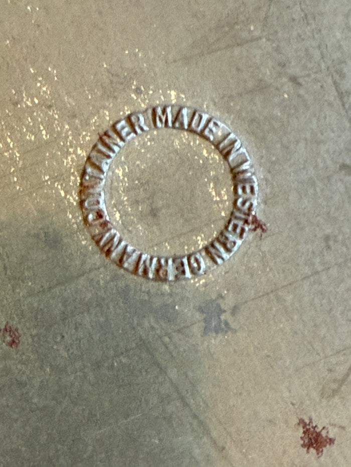 Circular metal stamp with 'Made in Western Germany' text on a textured surface