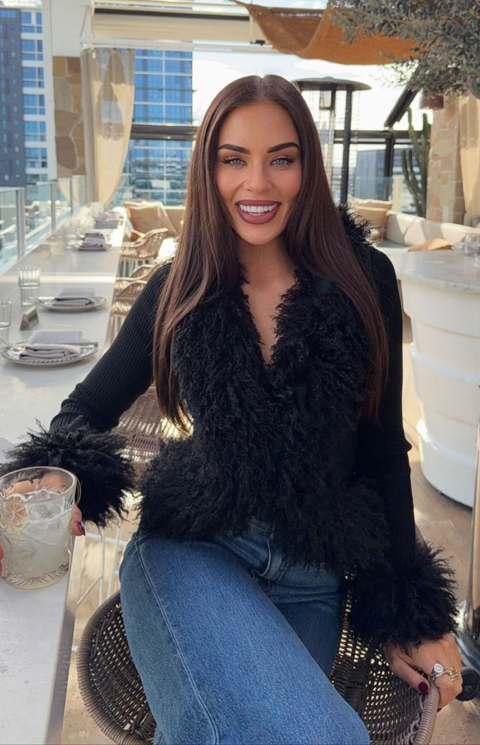 Front view of a black knit cardigan with shaggy fur trim on the V-neck and cuffs, ribbed sleeves