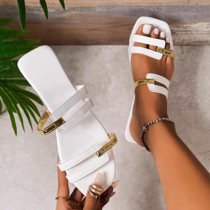 White sandals with gold buckles worn by a person on a neutral background