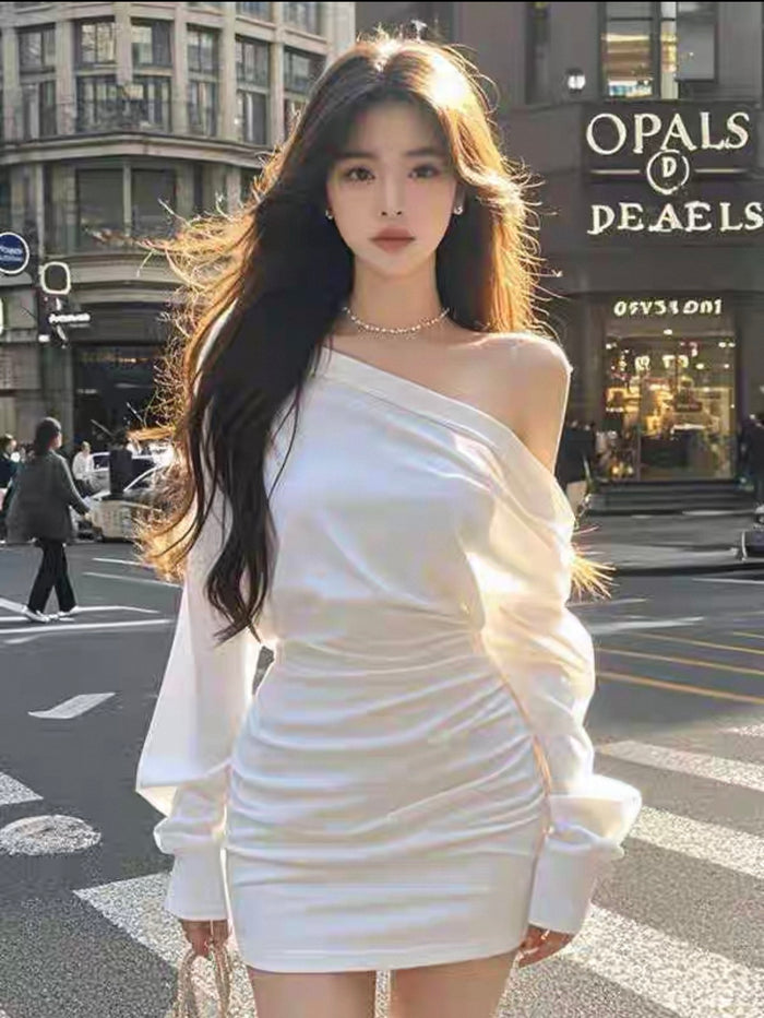 Woman in a white one-shoulder dress standing on a city street with 'Opals' and 'Deaels' shops in the background.
