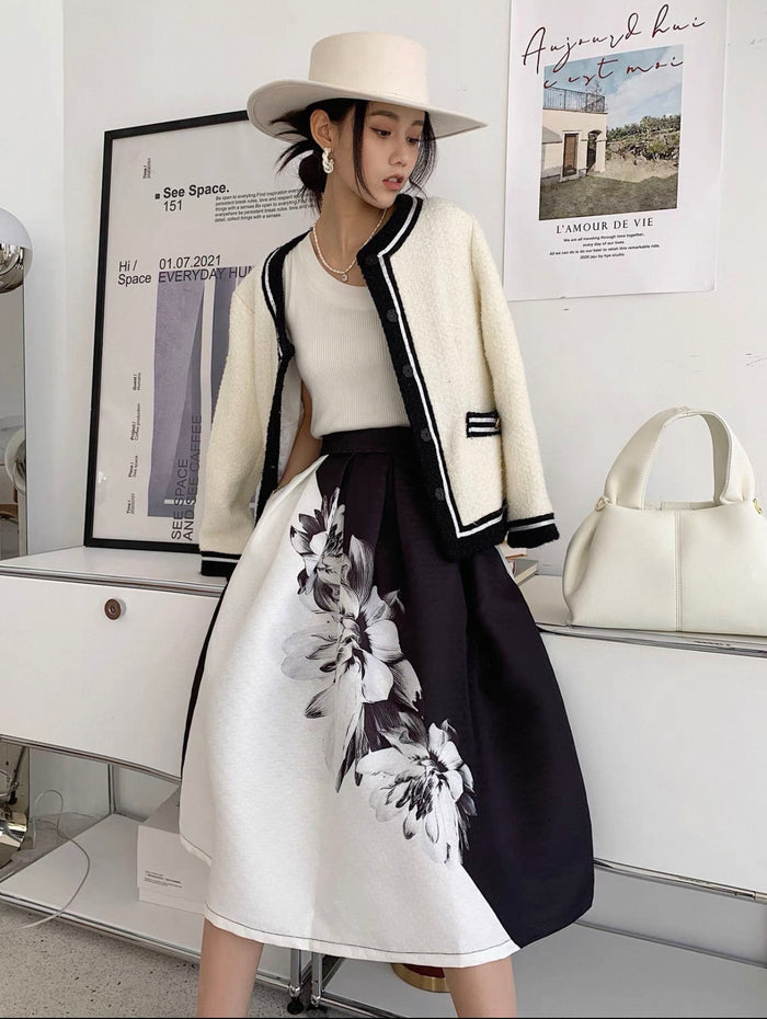 Woman wearing a stylish outfit with a white jacket, black and white floral skirt, and white hat in an indoor setting.