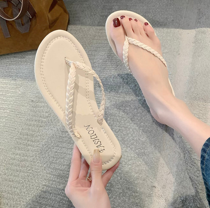 Beige sandals with braided straps held by a hand on a gray surface
