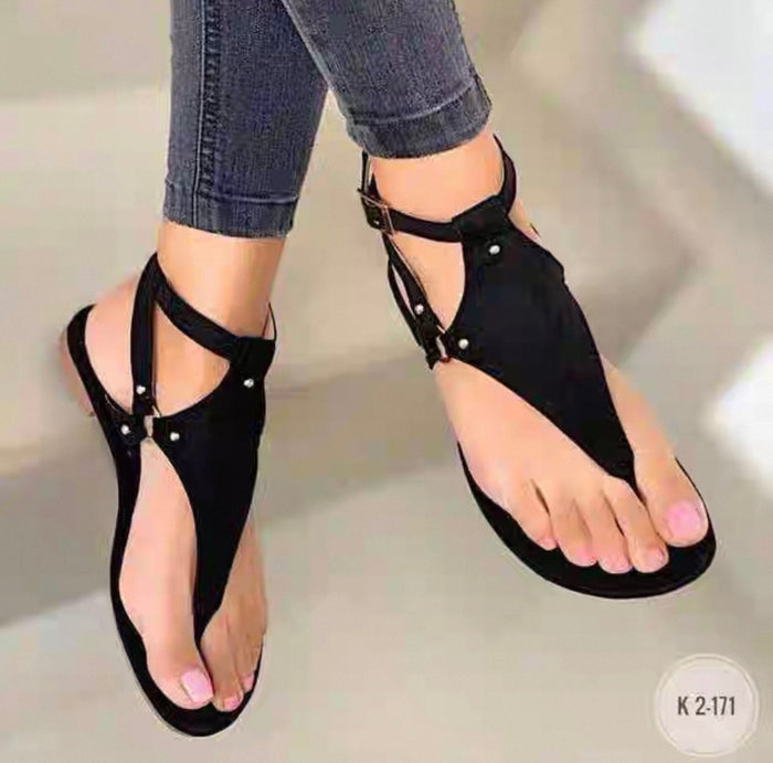 Black sandals worn with rolled-up jeans on a neutral background