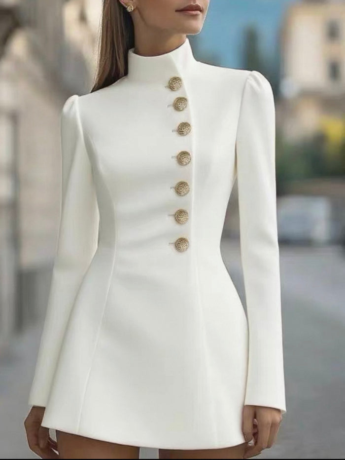 White dress with gold buttons worn by a model against a blurred outdoor background
