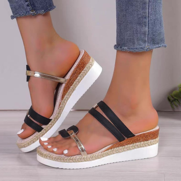 Wedges sandals with black straps and brown soles worn by a person on a neutral background