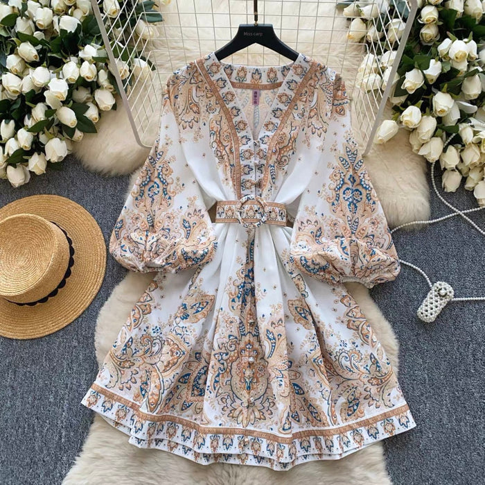Floral dress with a belt on a hanger surrounded by flowers and a hat.
