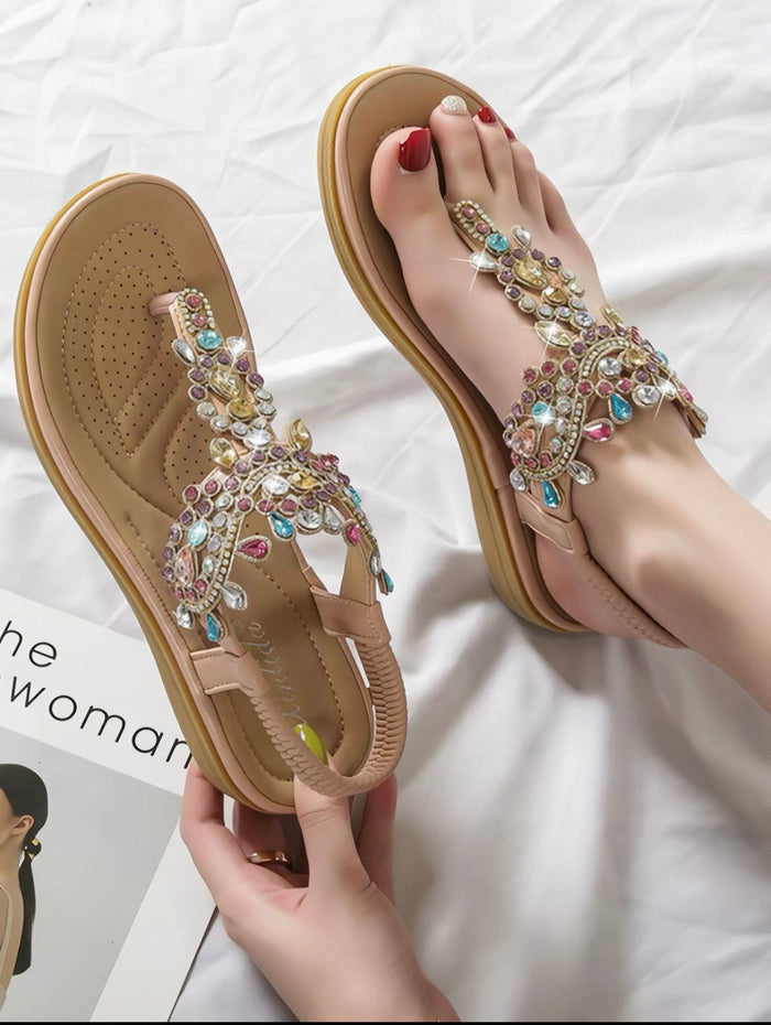 Beige sandals with colorful gemstones held by a hand on a white background