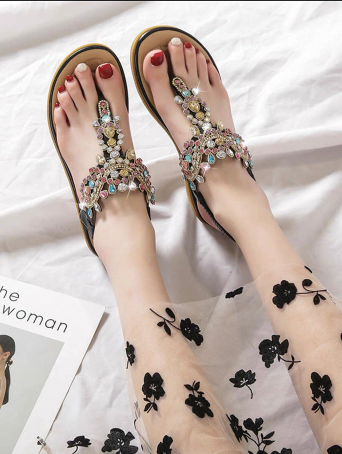 Beaded sandals worn with sheer black floral leggings on a white background
