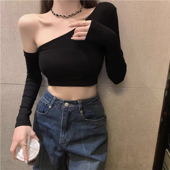 Person wearing a black one-shoulder top and blue jeans against a neutral wall.