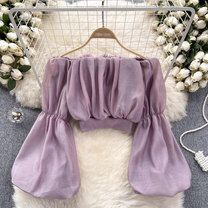 Purple off-shoulder top on a hanger with decorative flowers and fur rug in the background