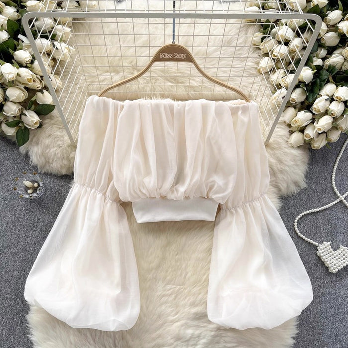 White off-shoulder top on a hanger with decorative flowers and pearls in the background