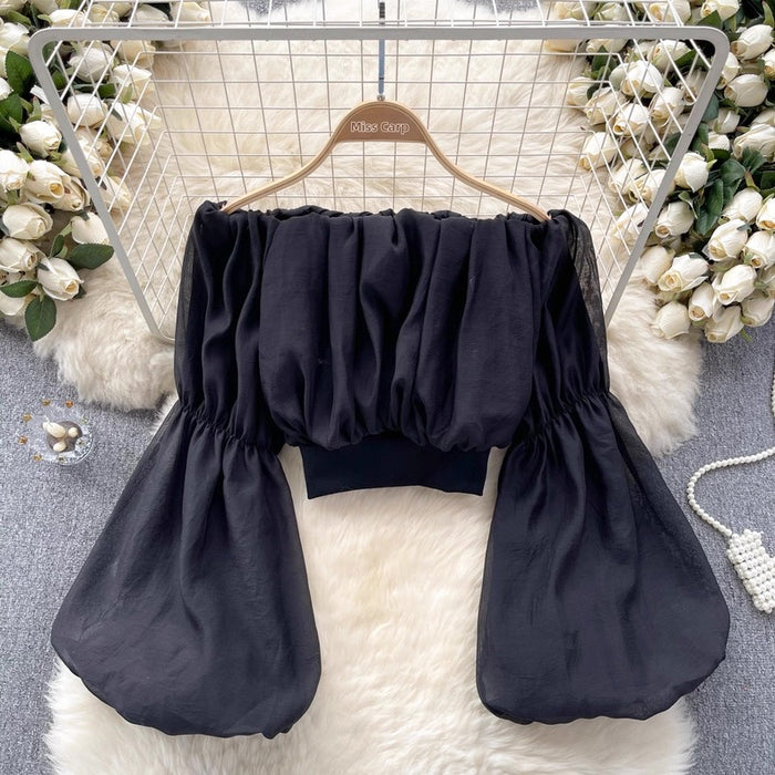 Black off-shoulder top on a hanger with decorative flowers and fur rug in the background