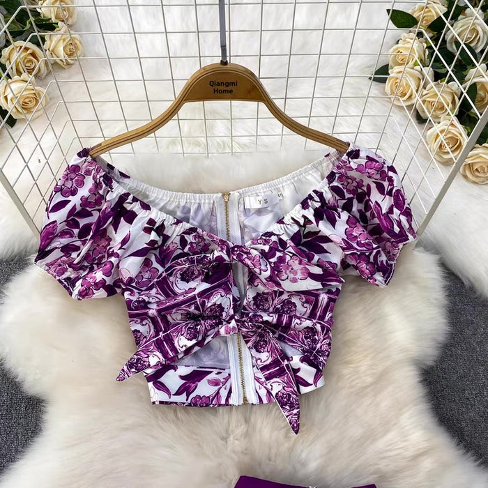 Purple floral off-shoulder top on a hanger with flowers in the background