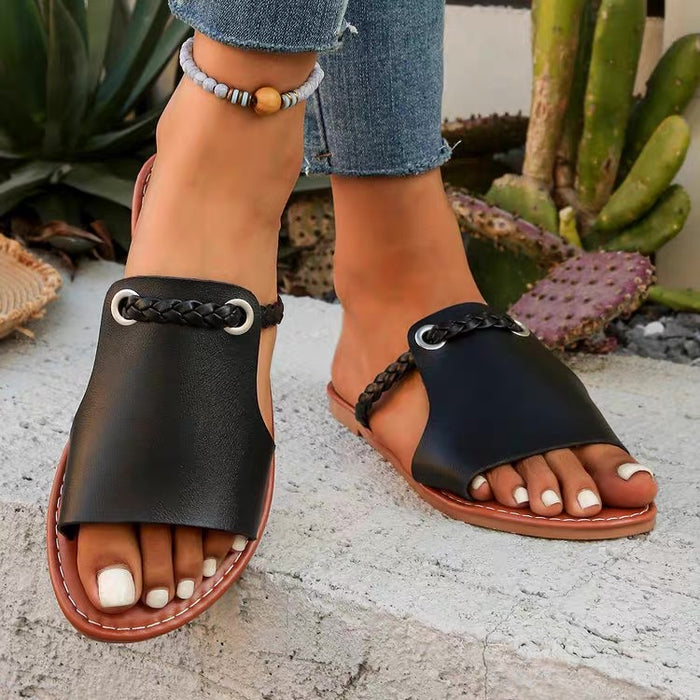 Black sandals with brown soles worn by a person, with cacti in the background.