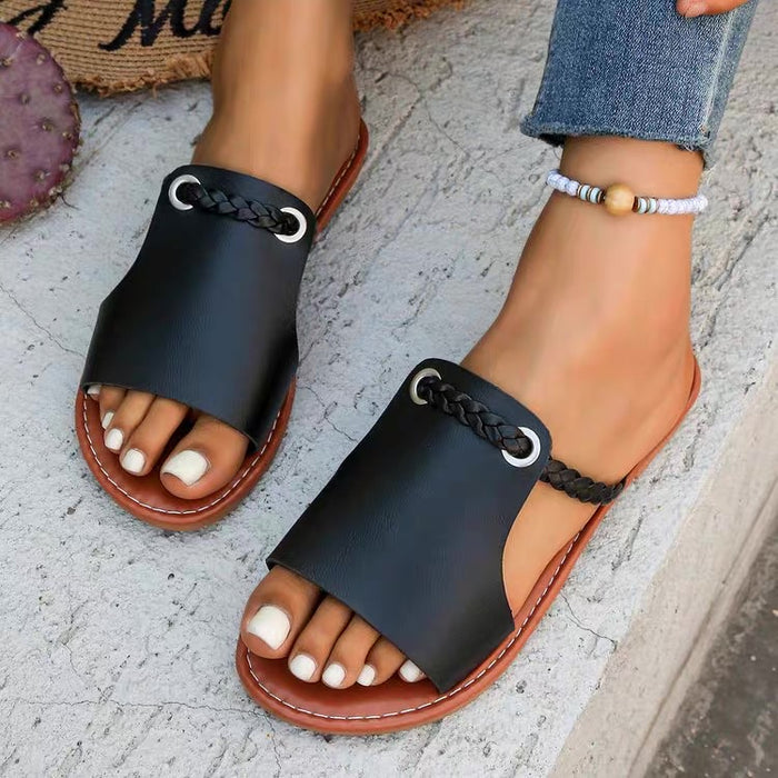 Black sandals with brown soles worn by a person on a textured surface