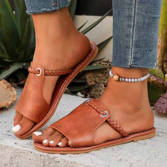Brown sandals worn with denim jeans on a textured surface with plants in the background