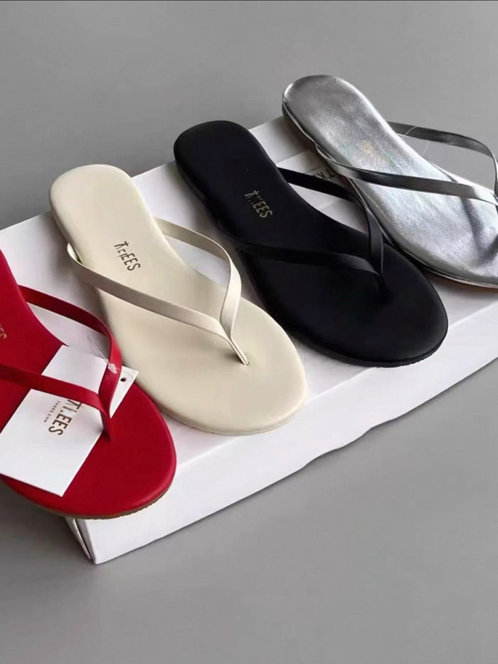 Four pairs of flip-flops in red, white, black, and silver on a gray surface.