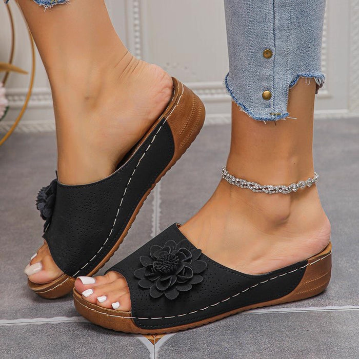 Black sandals with floral details worn by a person on a neutral background
