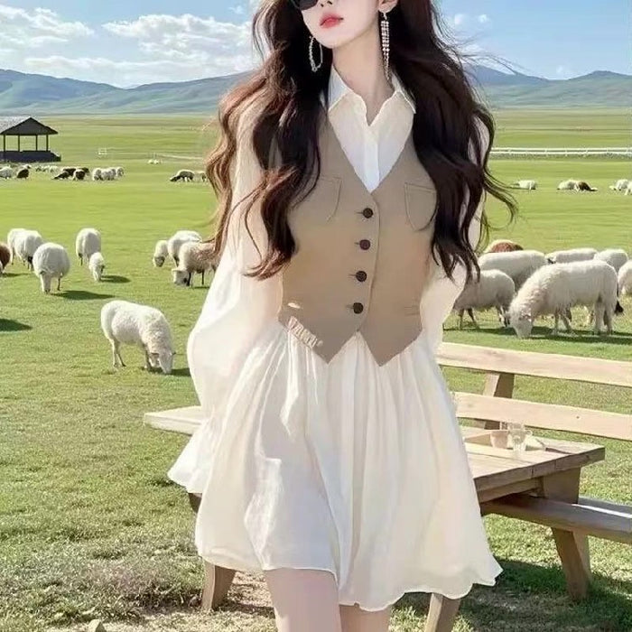 Woman in a white dress with a beige vest standing in a pastoral setting with sheep and mountains.